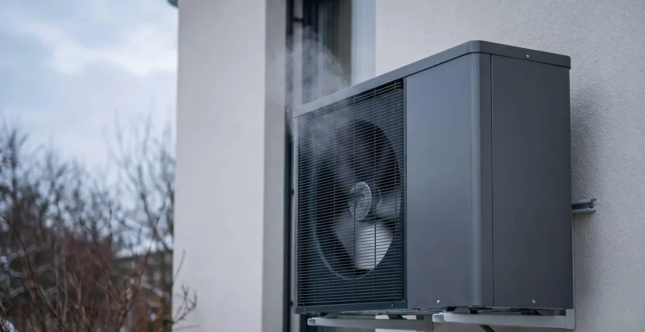 Gros plan sur une pompe à chaleur air-eau moderne en fonctionnement installée contre un mur extérieur, avec de la vapeur s'échappant en hiver