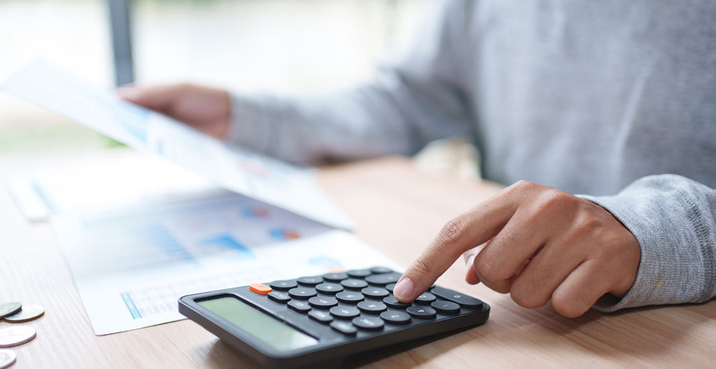 Personne d'âge mûr examinant des avis d'imposition et relevés de revenus fonciers sur un bureau domicile contemporain, calculatrice et ordinateur portable visibles, concentration sur documents fiscaux